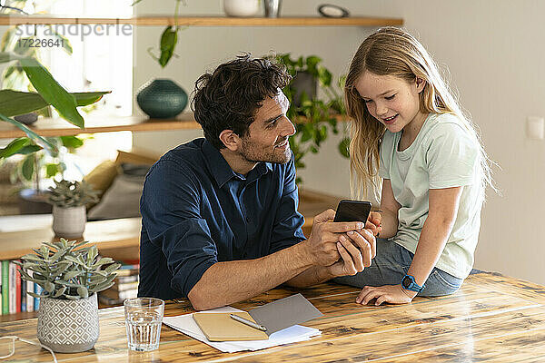 Mann zeigt seiner Tochter das Smartphone  während er zu Hause darüber diskutiert