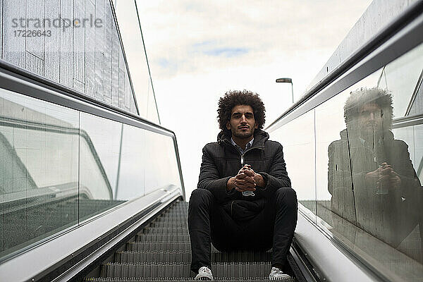 Gutaussehender Afro-Mann sitzt auf Rolltreppe am Himmel