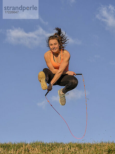 Junge Frau springt Seil vor blauem Himmel