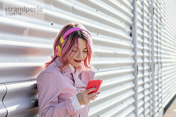 Lächelnde Frau  die an einem sonnigen Tag ein Mobiltelefon benutzt