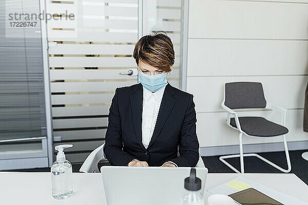 Geschäftsfrau mit Gesichtsschutzmaske bei der Arbeit am Laptop im Büro