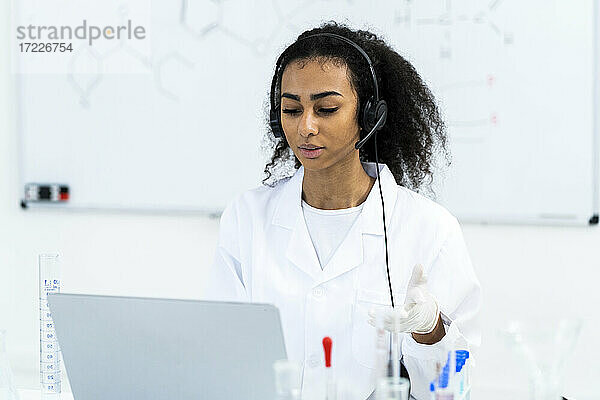 Junge Forscherin mit Headset bei einem Videogespräch über einen Laptop im Labor