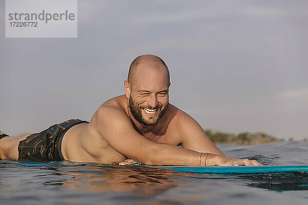 Lächelnder männlicher Surfer auf einem Surfbrett an einem sonnigen Tag