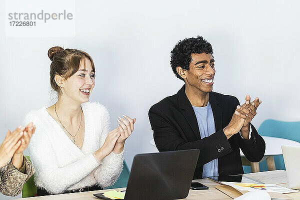 Lächelnde Kollegen  die bei einer Besprechung im Büro in die Hände klatschen