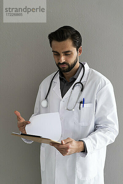 Männlicher Arzt liest medizinischen Bericht vor einer Wand