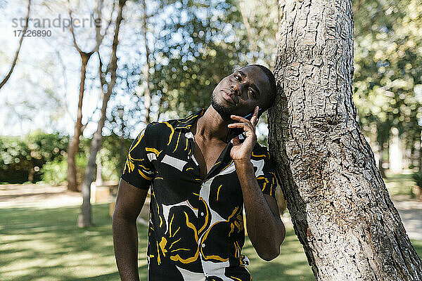 Junger Mann telefoniert an einem Baum an einem sonnigen Tag