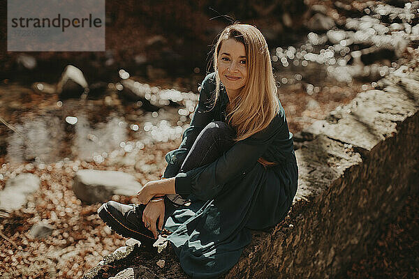 Schöne Frau sitzt im Herbst auf einer Stützmauer