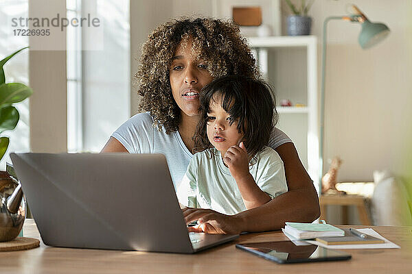 Mutter und kleine Tochter schauen gemeinsam auf den Laptop  während sie von zu Hause aus arbeiten