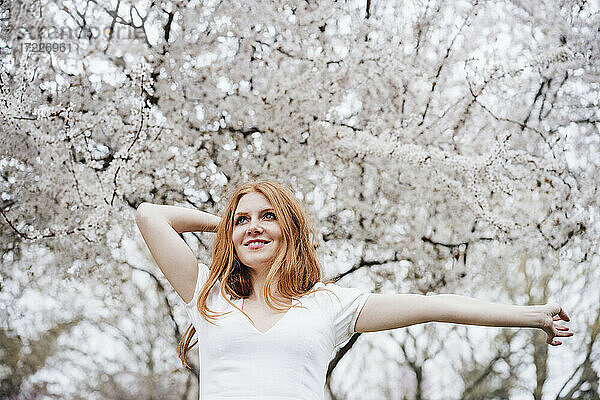 Glückliche junge Frau tanzt vor einem Mandelbaum und schaut dabei weg