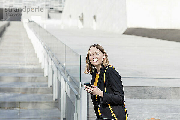 Lächelnde Geschäftsfrau mit Mobiltelefon im Treppenhaus