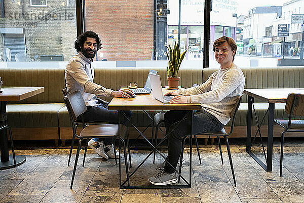 Glücklicher männlicher Unternehmer mit Laptop am Schreibtisch sitzend im Büro