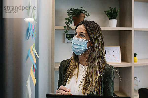 Konzentrierte Geschäftsfrau mit Gesichtsschutzmaske bei der Arbeit im Büro