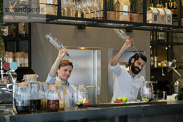 Gut aussehender Barkeeper und Auszubildender gießen Alkohol in ein Fruchtglas am Bartresen