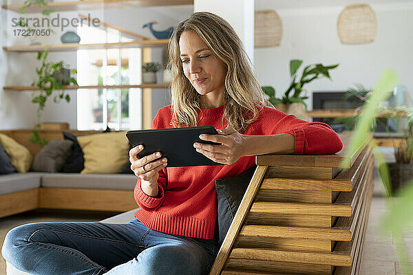 Frau benutzt digitales Tablet  während sie auf der Couch im Wohnzimmer sitzt