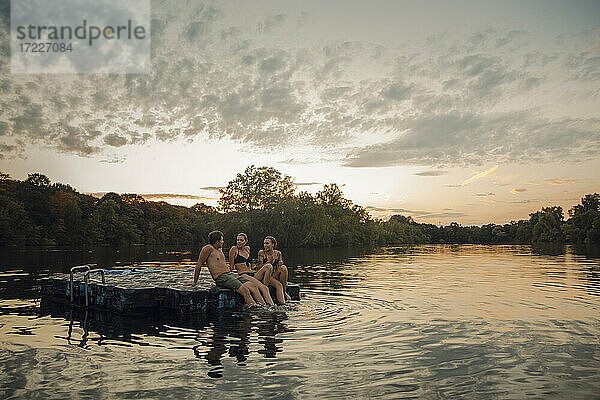 Freunde  die sich am See vergnügen  auf einer Badeplattform sitzend