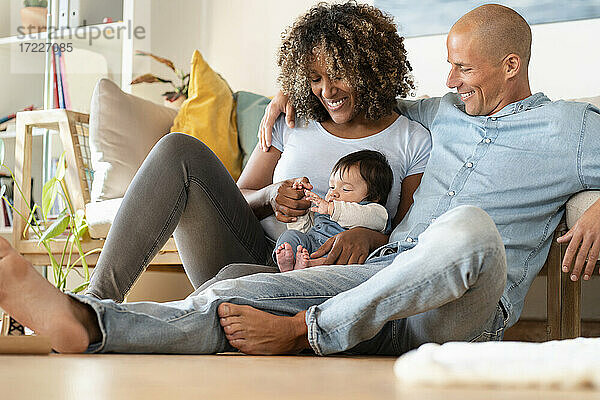 Lächelnde Mutter und Vater betrachten das Baby  während sie zu Hause auf dem Boden sitzen
