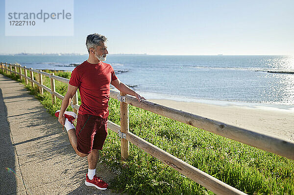 Mann streckt sich in der Nähe des Geländers am Strand an einem sonnigen Tag am Meer