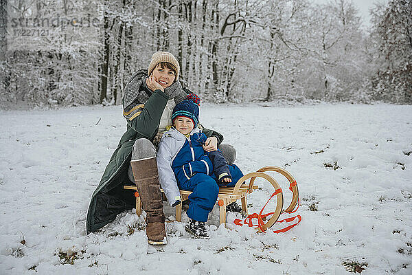 Mutter und Sohn sitzen auf einem Schlitten auf einem verschneiten Feld im Winter