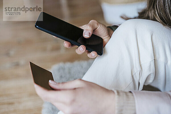 Hände einer Frau  die ein Smartphone benutzt  während sie zu Hause mit einer Kreditkarte bezahlt