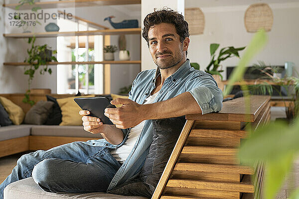 Gutaussehender Mann mit digitalem Tablet auf der Couch im Wohnzimmer sitzend