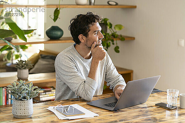Nachdenklicher Freiberufler  der wegschaut  während er mit seinem Laptop im Heimbüro sitzt