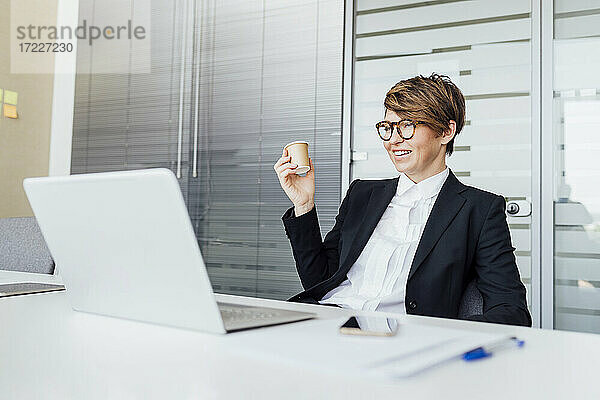 Lächelnde Geschäftsfrau  die einen Kaffee trinkt und auf einen Laptop am Schreibtisch schaut