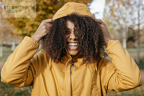 Fröhliche Afro-Frau mit Jackenkapuze im Park im Herbst