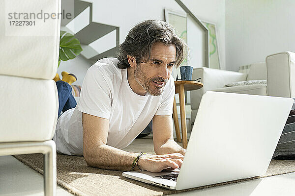 Mann benutzt Laptop  während er zu Hause auf dem Boden liegt