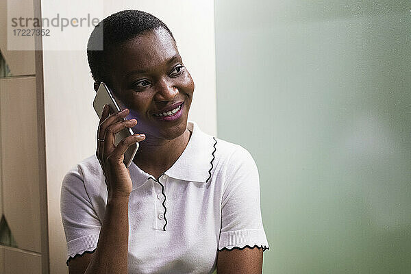 Lächelnde Geschäftsfrau  die in einem kreativen Büro mit einem Mobiltelefon spricht