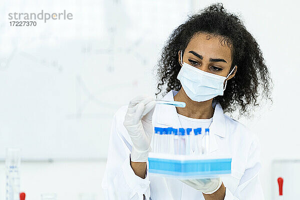 Forscherin mit Gesichtsschutz bei der Untersuchung einer Flüssigkeit im Reagenzglas während der Arbeit im Labor