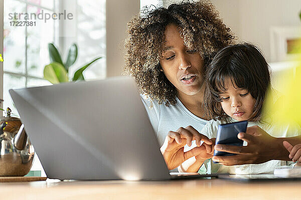 Mutter  die im Home-Office mit ihrer Tochter am Smartphone arbeitet und dabei Multitasking betreibt