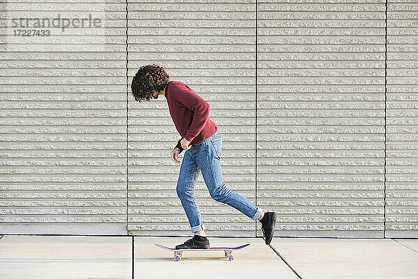 Lockenhaariger Mann fährt mit dem Skateboard an der Wand