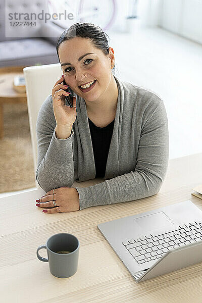 Lächelnde Geschäftsfrau  die bei der Arbeit zu Hause ein Mobiltelefon benutzt