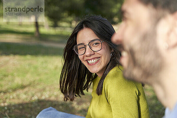 Fröhliche Frau mit Brille sieht ihren Freund an  während sie sich in einem öffentlichen Park amüsiert