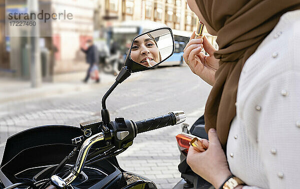 Junge Frau trägt Lippenstift auf und schaut in den Motorradspiegel