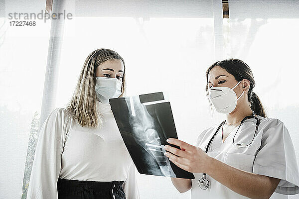 Ärztin zeigt einem Patienten in der Klinik ein Röntgenbild während COVID-19