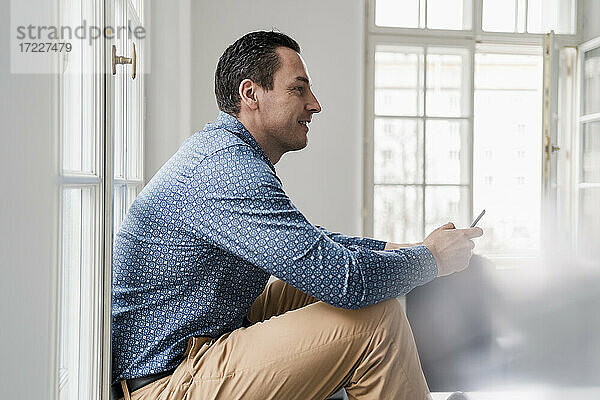 Männlicher Unternehmer  der im Büro sitzend ein Smartphone benutzt