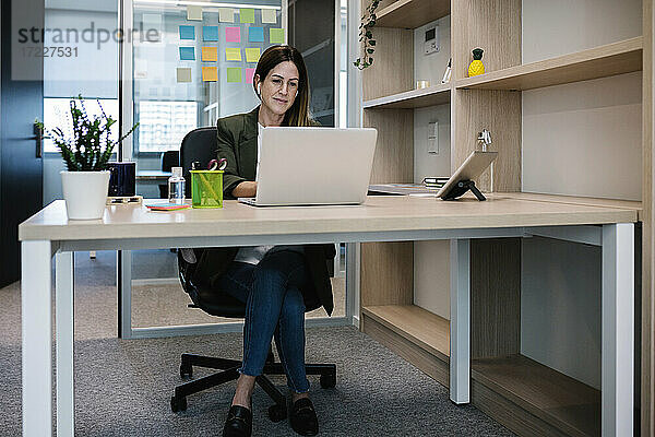 Konzentrierte Unternehmerin arbeitet am Laptop  während sie am Schreibtisch im Büro sitzt