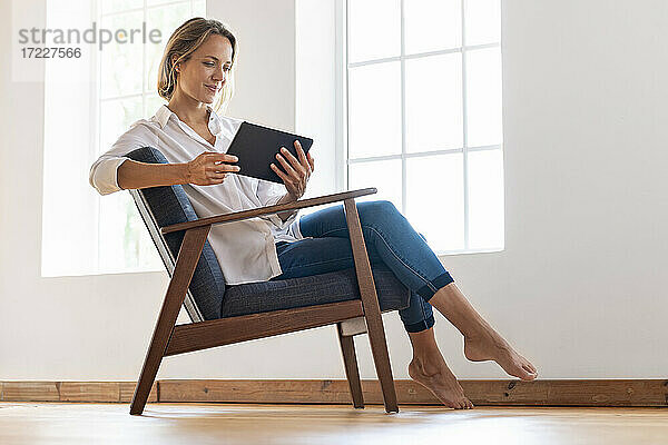 Frau sitzt auf einem Sessel und schaut auf ein digitales Tablet