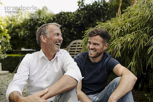 Vater und Sohn lachen  während sie zusammen im Garten sitzen
