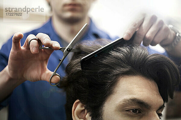Hände eines Friseurs  der einem männlichen Kunden die Haare schneidet