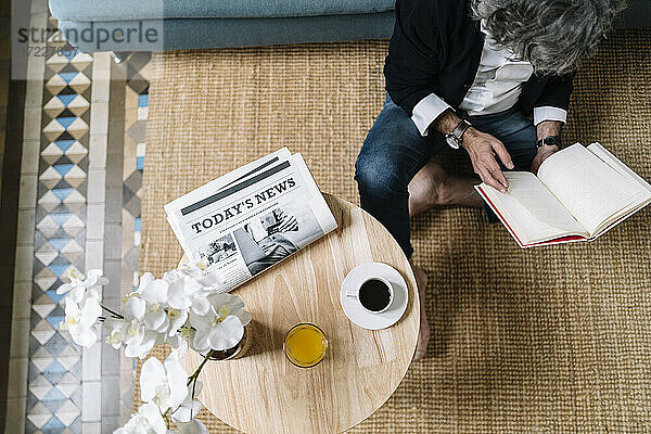 Mann  der ein Buch liest  während Kaffee und Saft auf einem Holztisch zu Hause stehen