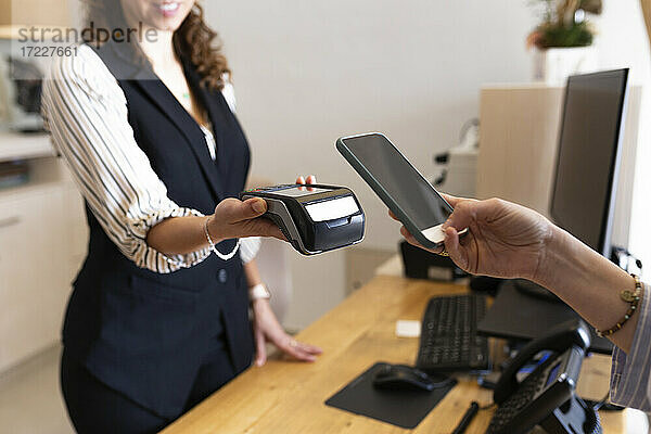 Geschäftsfrau hält Mobiltelefon an Kreditkartenleser an der Hotelrezeption