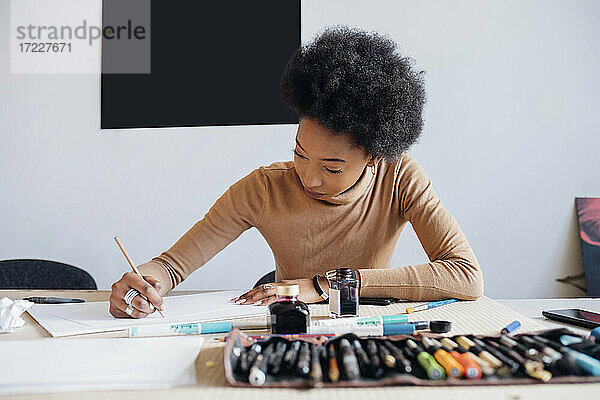 Afro-Frau schreibt mit Stift auf Papier  während sie an einem Tisch im Studio sitzt