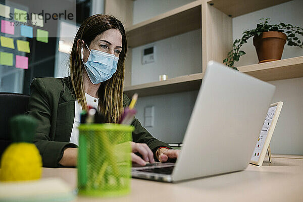 Geschäftsfrau mit Schutzmaske bei der Arbeit am Laptop im Büro während einer Pandemie