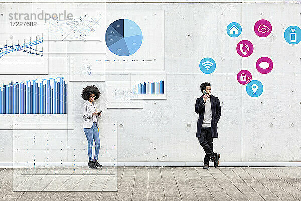 Geschäftsfrau und Mann mit Mobiltelefon stehen vor einer Grafik  einem Diagramm und einem Symbol auf einem Fußweg