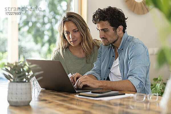 Mann benutzt Laptop  während er mit seiner Freundin am Tisch sitzt