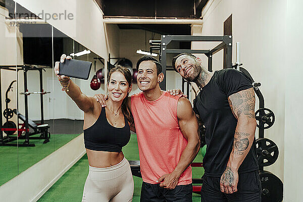 Lächelnde Sportlerin  die ein Selfie mit ihren männlichen Freunden im Fitnessstudio macht