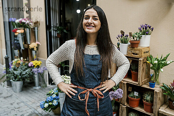 Lächelnde junge Blumenhändlerin  die mit den Händen auf den Hüften in einem Blumenladen steht