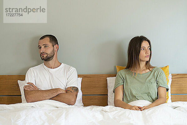 Frustriertes junges Paar sitzt auf dem Bett und schaut sich zu Hause gegenseitig an